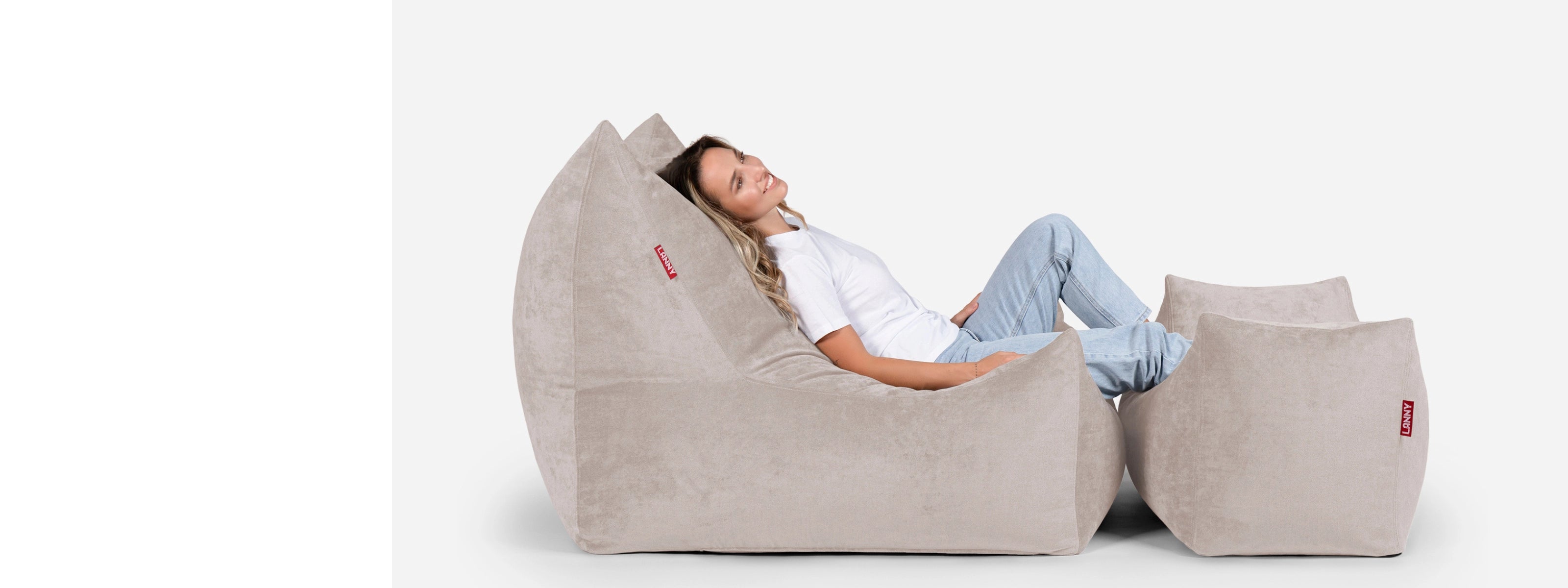 Person relaxing on a Lanny large beige bean bag chair with smaller bean bags on a white background