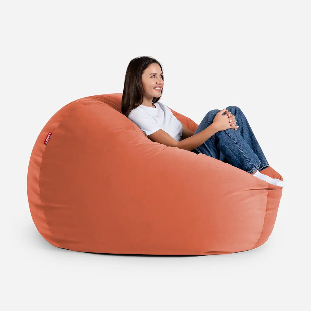 Woman relaxing on a Lanny Sphere amber orange velvet bean bag chair, showing the large size and comfortable back support