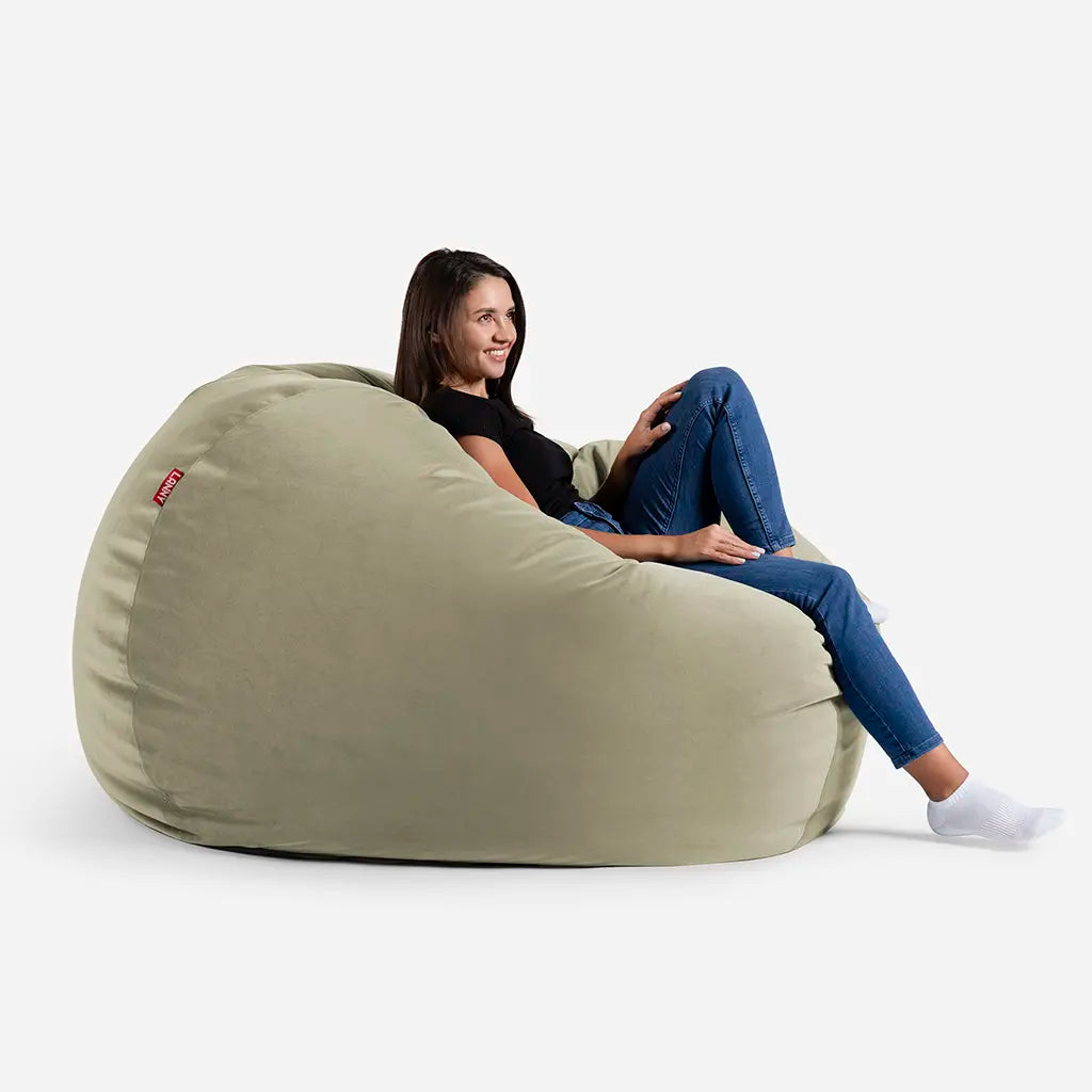 Woman relaxing on a Lanny Sphere khaki green velvet bean bag chair, showing the large size and comfortable back support