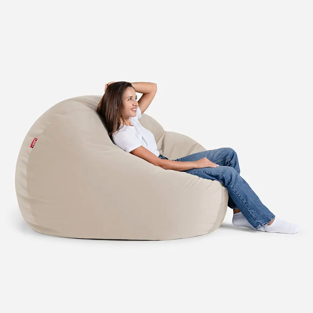 Woman relaxing on a Lanny Sphere beige velvet bean bag chair, showing the large size and comfortable back support