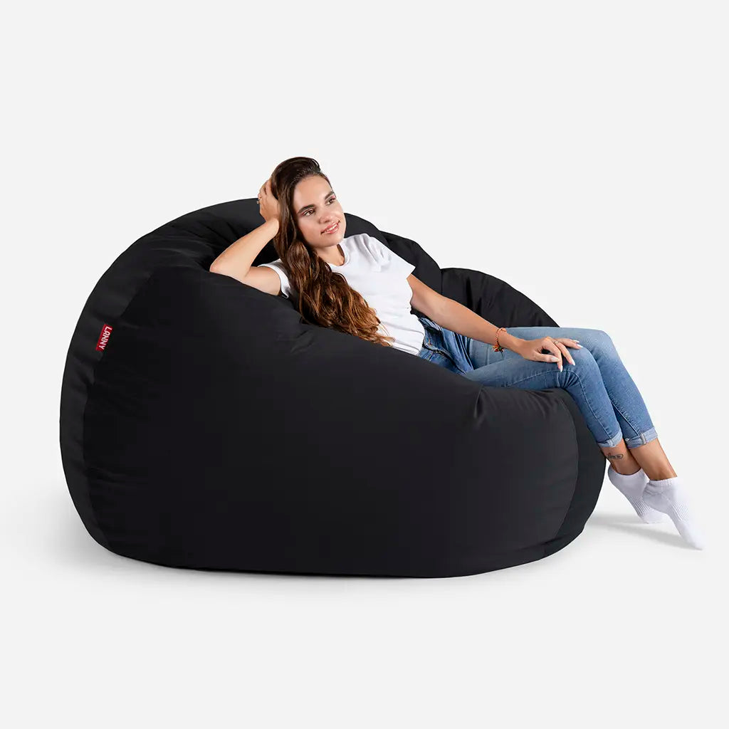 Woman relaxing on a Lanny Sphere black velvet bean bag chair, showing the large size and comfortable back support