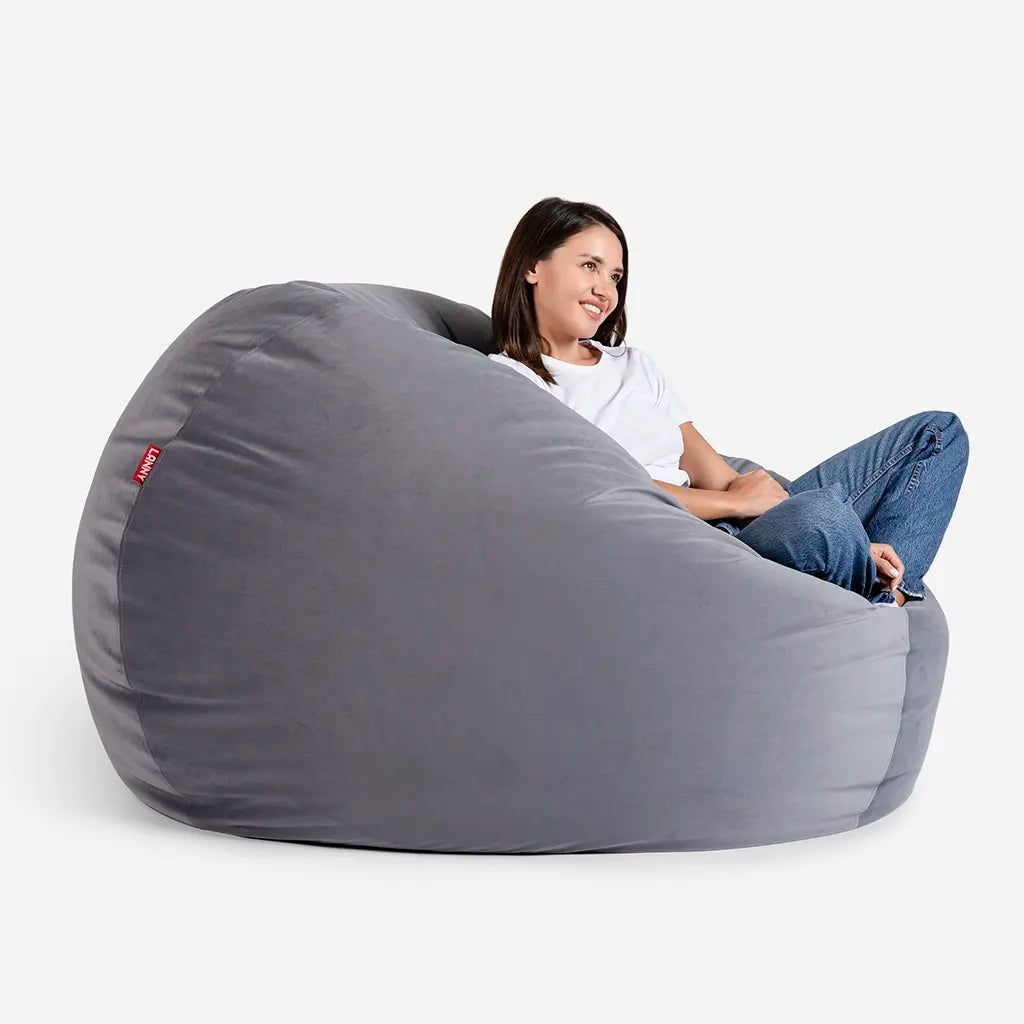 Woman relaxing on a Lanny Sphere gray velvet bean bag chair, showing the large size and comfortable back support
