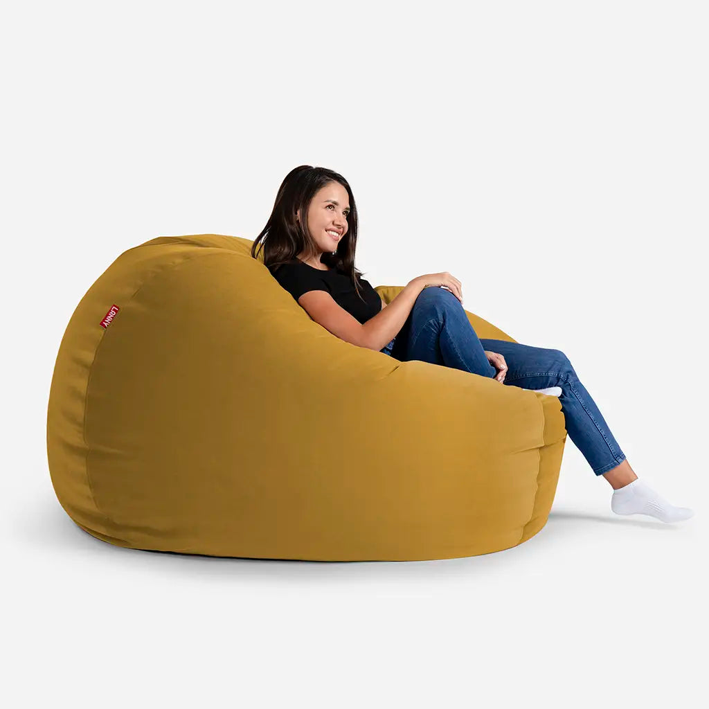 Woman relaxing on a Lanny Sphere Mustard yellow velvet bean bag chair, showing the large size and comfortable back support