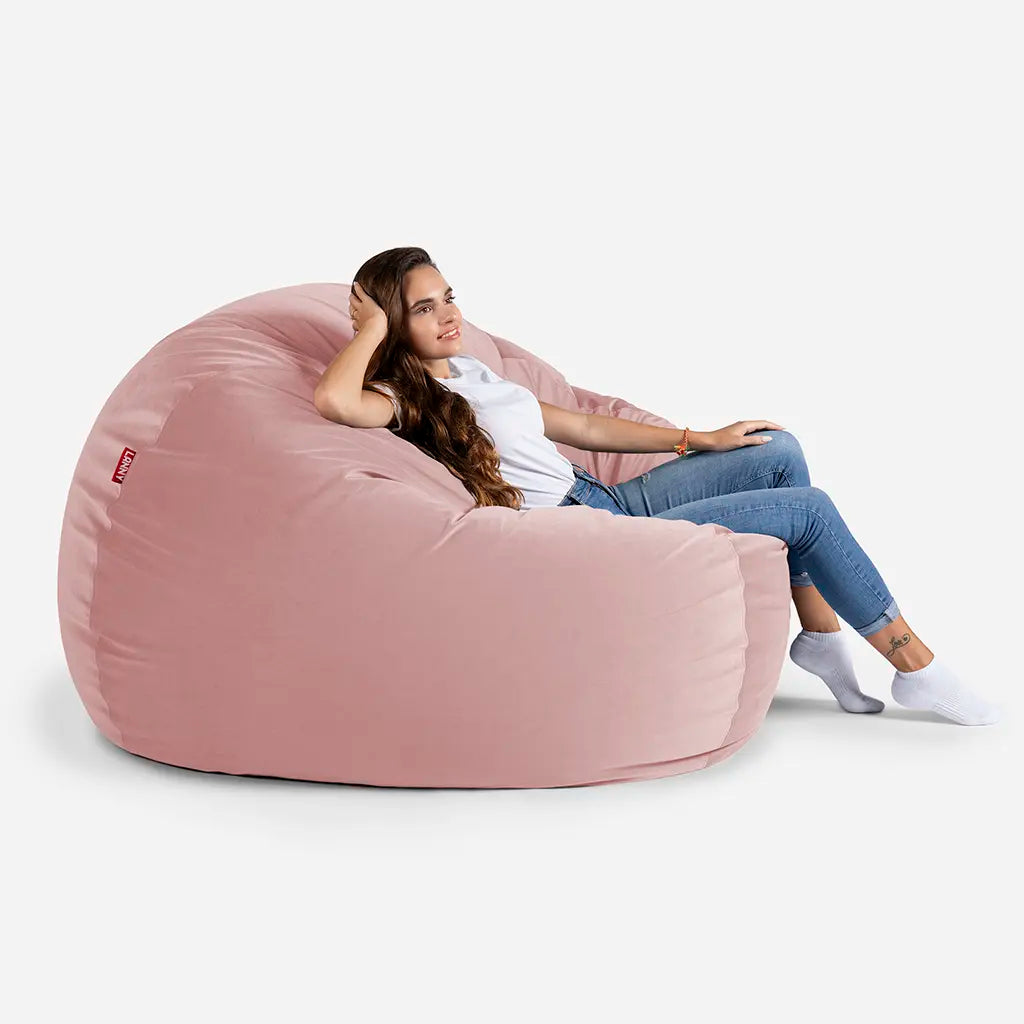 Woman relaxing on a Lanny Sphere Pink velvet bean bag chair, showing the large size and comfortable back support